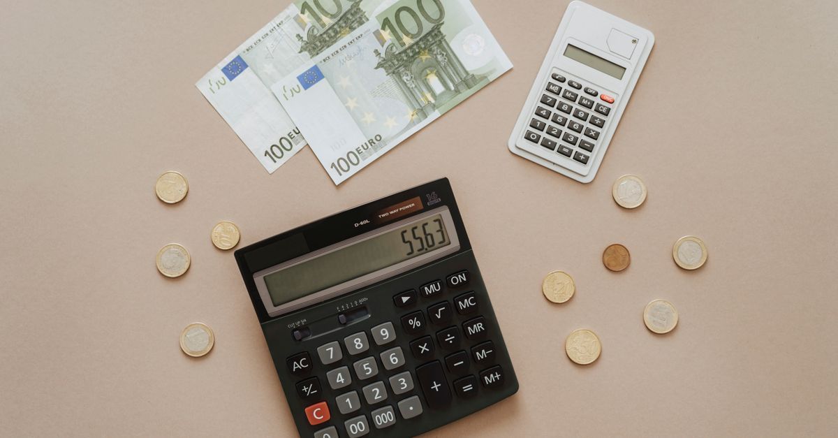 Billetes de cien euros, monedas y dos calculadoras sobre un fondo liso.